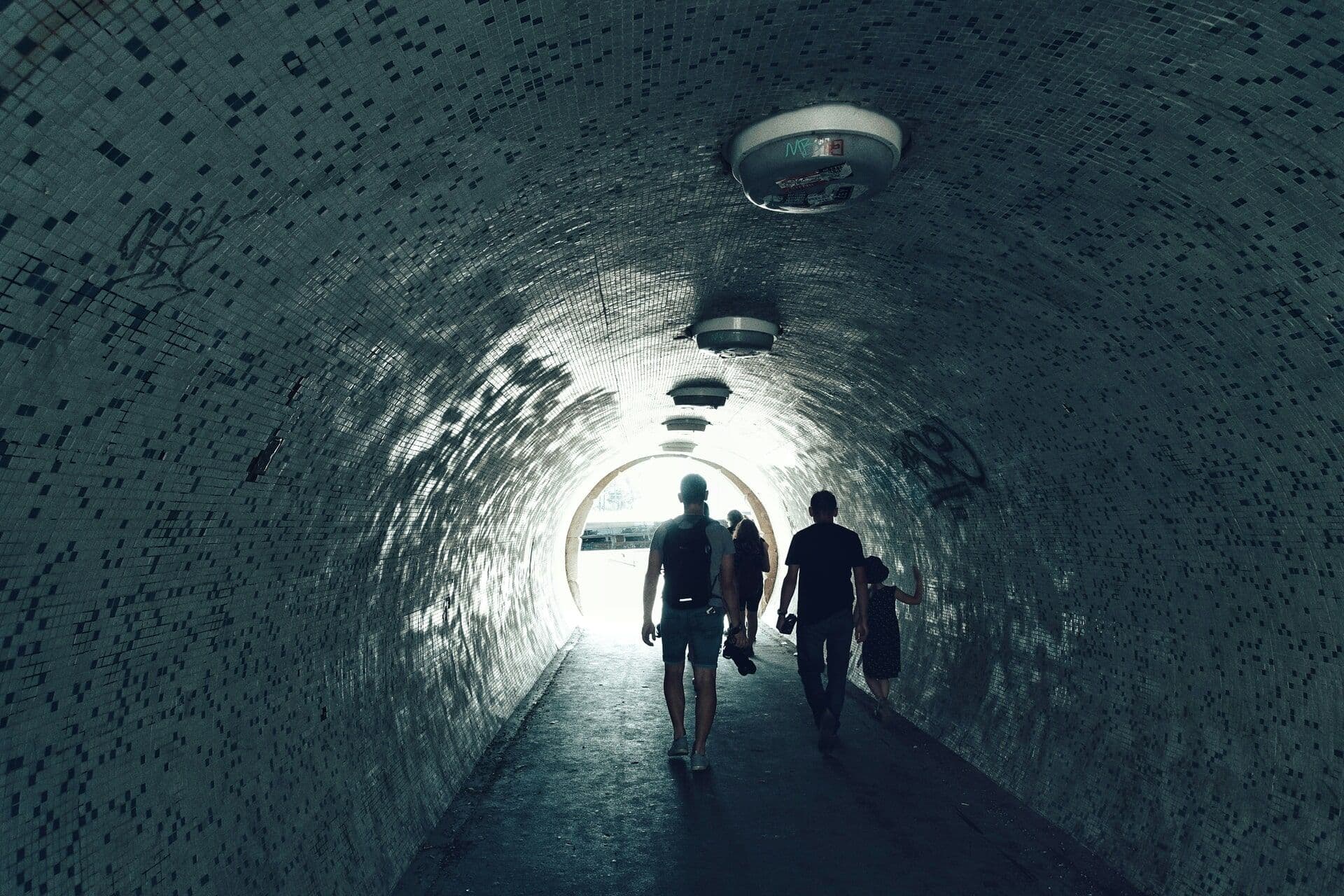 people walking through a dark tunnel toward the light